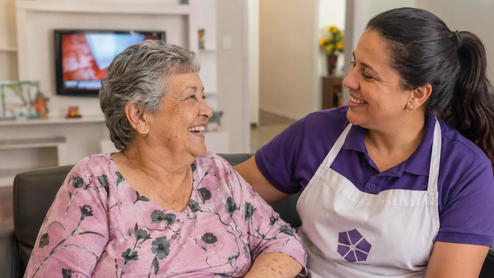 Residente idosa e cuidadora sorriem durante momento de convivência, imagem ilustrativa